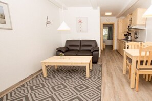A compact living space with a sofa, a small table, a kitchen area, and a patterned floor. - Terraced house - 1 bedroom - 40 sqm (Ostseebad Rerik)