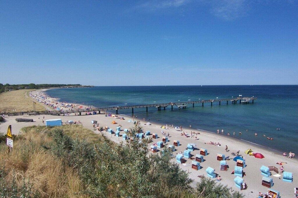 Ein Strand mit einem Steg, der sich ins Wasser erstreckt, Liegestühlen und Sonnenschirmen.
