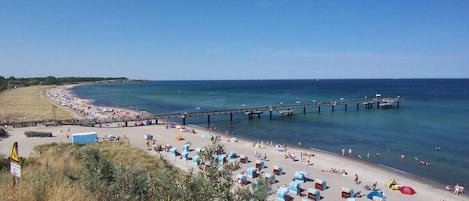 A beach with a pier extending into the water, beach chairs, and umbrellas.