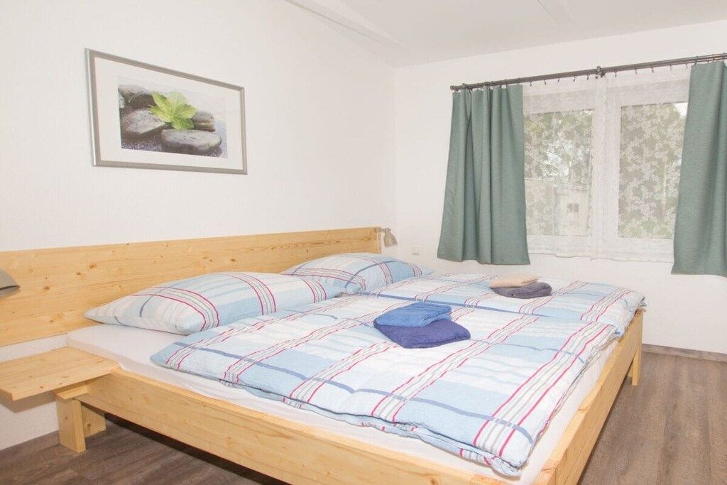 Un lit simple avec une tête de lit en bois, une table de chevet et une fenêtre avec des rideaux.