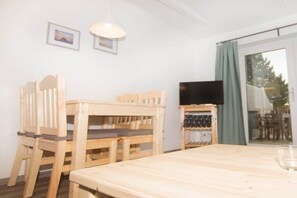 A room with a wooden table, two chairs, a television on a stand, and a sliding glass door leading to an outdoor area. - Terraced house - 1 bedroom - 40 sqm (Ostseebad Rerik)