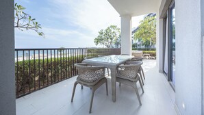 Een balkon met een glazen tafel en rieten stoelen, met uitzicht op een strand en een stadsbeeld.