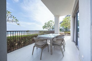 En balkon med et glasbord og fletstole, med udsigt over en strand og bybilledet.