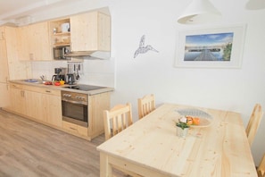 A kitchen with wooden cabinets, a stove, and a dining table with chairs. - Terraced house - 2 bedrooms - 55 sqm (Ostseebad Rerik)