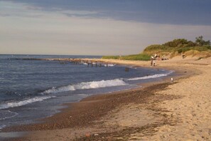 Ein Strand mit sandigem Ufer, Wellen und einigen Menschen in der Ferne.