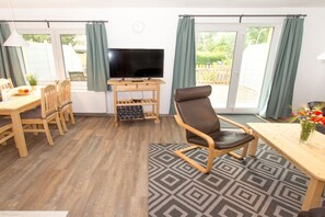 A furnished room with a television, a dining table, chairs, a sofa, and a patterned rug. - Terraced house - 2 bedrooms - 75 sqm (Ostseebad Rerik)