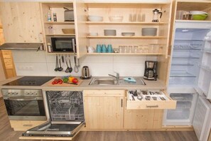 A compact kitchen with a microwave, oven, and dishwasher, wooden cabinets, and a built-in refrigerator. - Terraced house - 2 bedrooms - 75 sqm (Ostseebad Rerik)