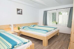 Ein Schlafzimmer mit zwei hölzernen Betten, einem Fenster mit Vorhängen und einem kleinen Wandbild.