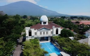 A large building with a dome and a swimming pool, surrounded by trees and a mountain in the background. - De Jehans Boutique Hotel (Cilimus)