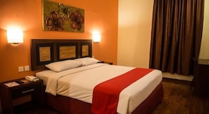 Habitación de hotel con cama, mesita de noche, un cuadro y ventana con cortinas.