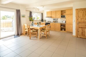 A kitchen with wooden cabinets, a dining table with chairs, and a sliding glass door leading to an outdoor area. - on the Baltic Sea - semi-detached house (Rerik)