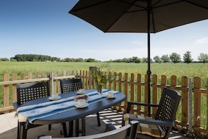 Une terrasse extérieure avec une table dressée pour deux personnes, une clôture en bois et une vue dégagée sur un champ verdoyant.
