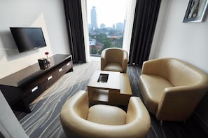 A hotel room with a flat-screen TV mounted on the wall, a sofa, a chair, and a small table. - Dreamtel Jakarta (Jakarta)