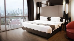 Una habitación de hotel moderna con una cama grande, vista a la ciudad y una silla roja.