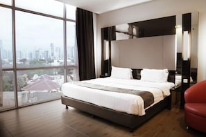 A modern hotel room with a large bed, a city view, and a red chair. - Dreamtel Jakarta (Jakarta)