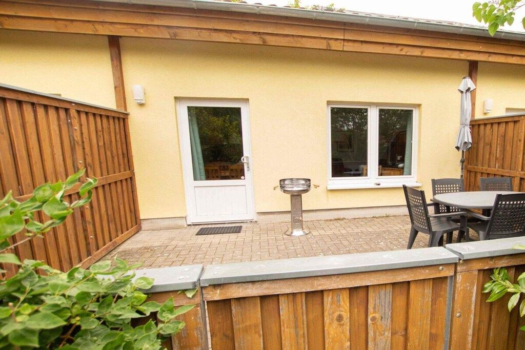 Een terras met een tafel, stoelen, een barbecue en een houten omheining.