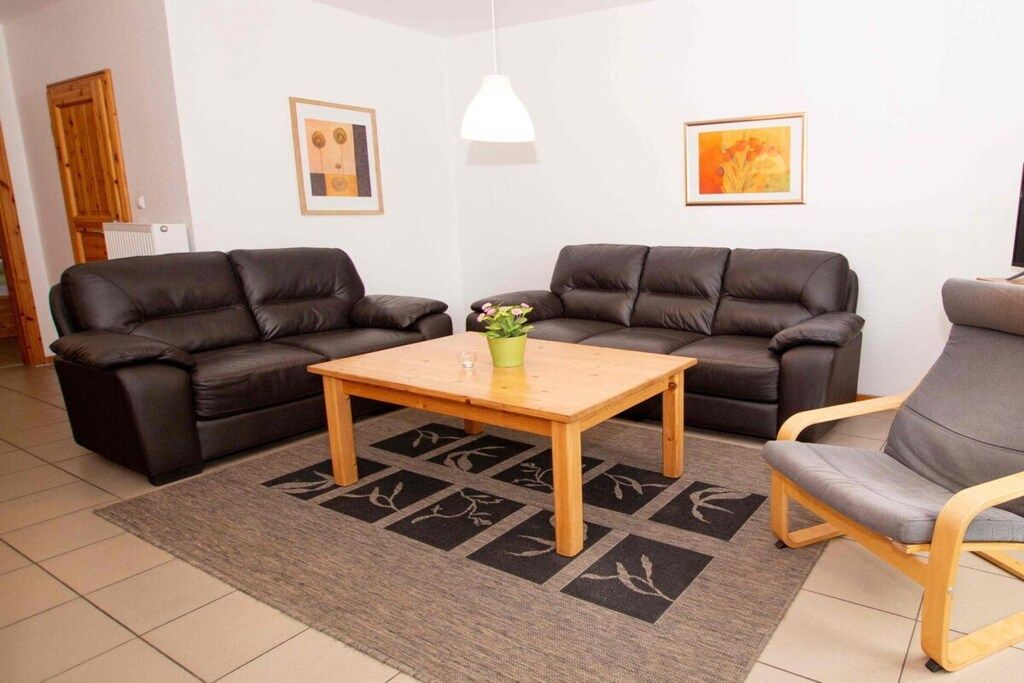 Ein Wohnzimmer mit zwei Sofas, einem Couchtisch und einem Sessel. An den Wänden hängen zwei gerahmte Bilder.