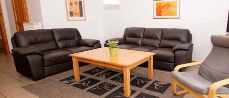 A living room with two sofas, a coffee table, and a chair. There are two framed pictures on the wall.