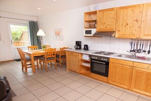 A kitchen with wooden cabinets, a dining table with chairs, a stove, a microwave, and a coffee maker. - Terraced house, 60 sqm, 2 bedrooms (Rerik)