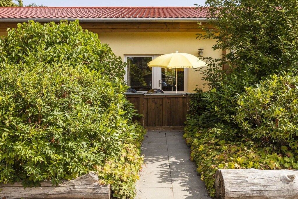 A pathway leading to a house with a yellow exterior, a wooden gate, and a yellow umbrella.