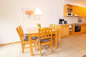 A compact kitchen with wooden cabinets, a dining table with chairs, and a hanging pendant light. - Terraced house, 60 sqm, 2 bedrooms (Rerik)