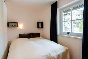 A hotel room with a bed, a window with curtains, and two wall-mounted light fixtures. - Solstice by Alpentravel (SW3) (Bad Gastein)