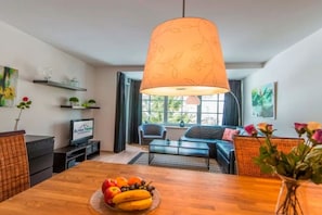 A modern living room with a wooden dining table, a fruit bowl, a sofa, and a large hanging lamp. - Solstice by Alpentravel (SW3) (Bad Gastein)