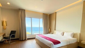 Habitación de hotel con una cama grande, una silla, una mesita de noche y vista al mar.