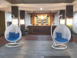 A reception area with a wooden counter, two white hanging chairs with blue cushions, and a patterned wall.