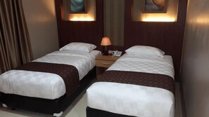 A hotel room with two beds, a nightstand, a lamp, and artwork on the walls.