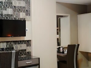A modern room with a flat-screen TV mounted on a wall with geometric patterns, a wooden desk with a chair, and a large mirror.