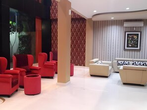 Un área de descanso moderna con sillones rojos, un sofá color crema y una pared con estampado.
