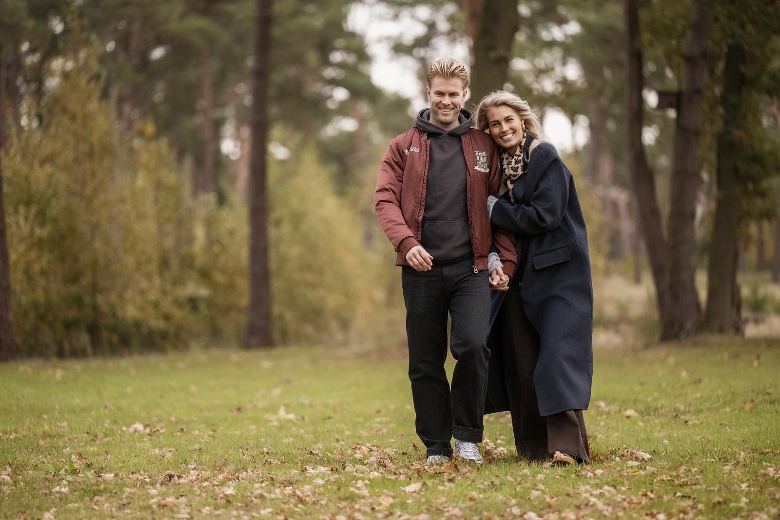 A couple walking in a park with trees and grass.