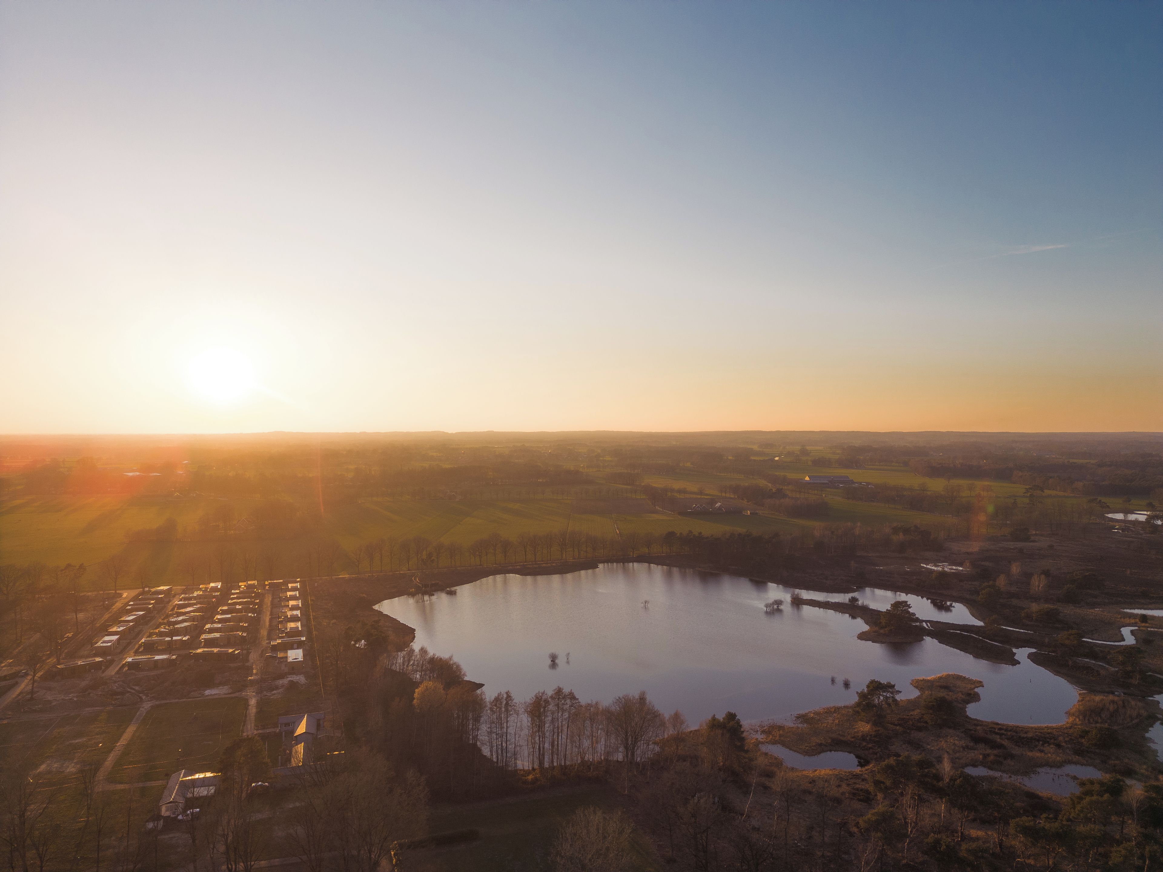 An aerial view of a landscape with a large body of water surrounded by fields and a few buildings.