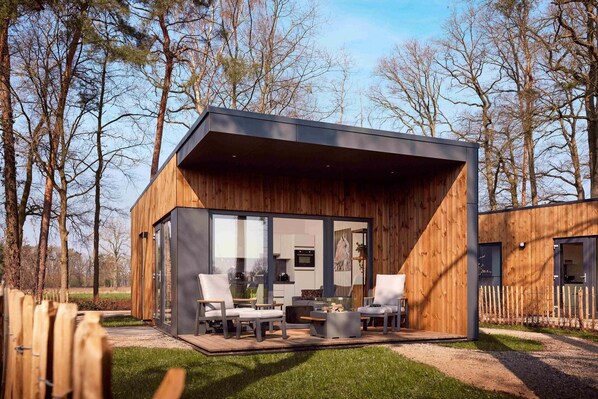 Une cabane moderne en bois dotée d’un patio vitré, aménagé avec des chaises et une table.
