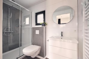 Une salle de bain moderne avec une douche à parois de verre, des toilettes, un lavabo avec un miroir au-dessus et une plante en pot posée sur le comptoir.