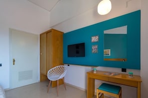 Una stanza con un'armadio in legno, una sedia bianca, una scrivania con specchio e un televisore appeso al muro.