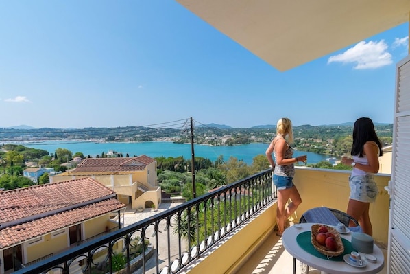 Un balcone con vista su un lago e montagne, un tavolo con un cesto di frutta e una ringhiera.