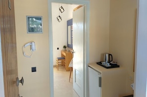 Una porta che dà su una stanza con una scrivania, una sedia e un angolo cottura con una macchina da caffè.
