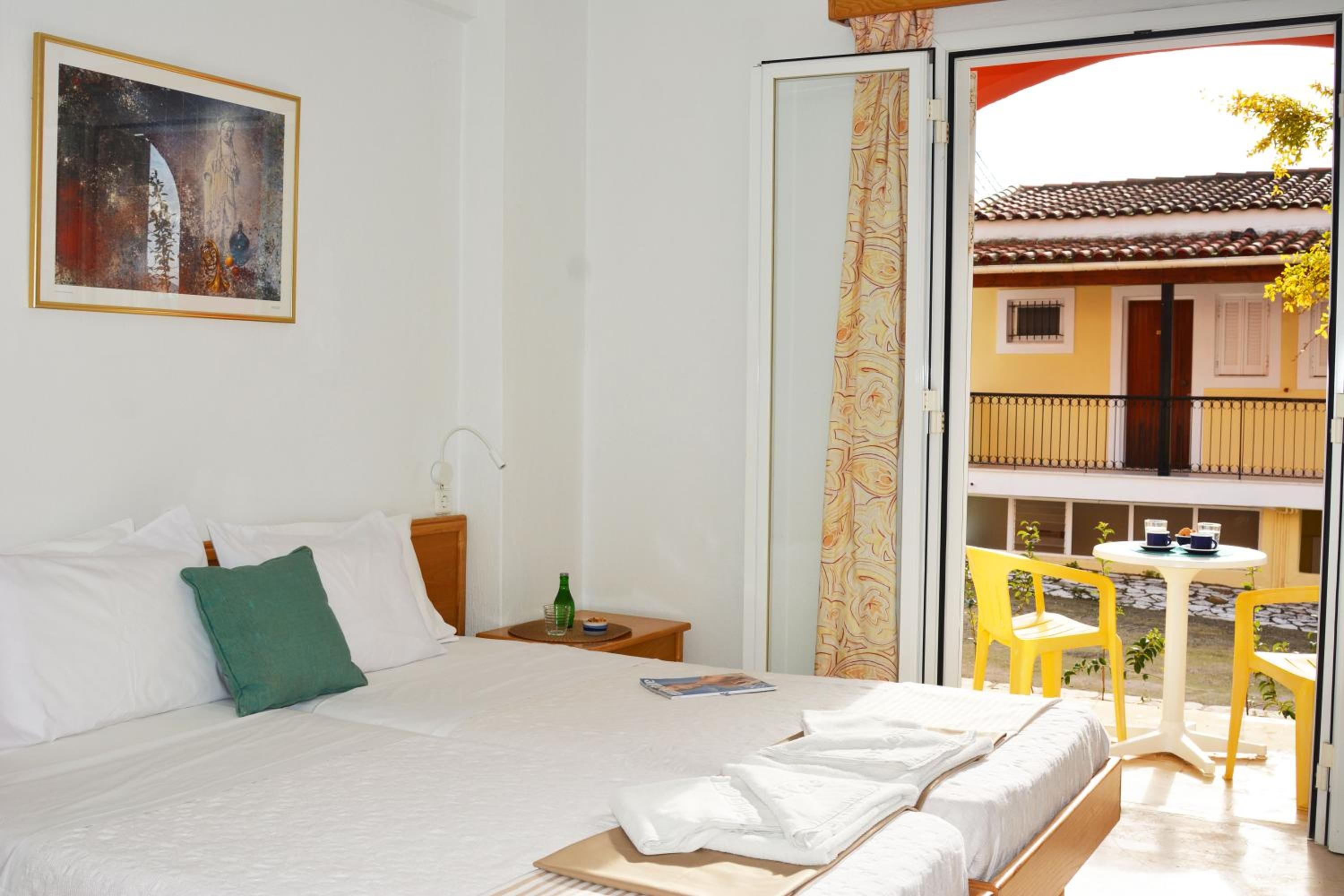 A hotel room with a bed, a nightstand, a painting, and a view of the outside balcony.