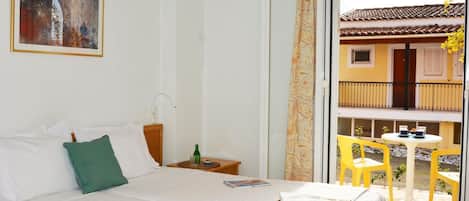 A hotel room with a bed, a nightstand, a painting, and a view of the outside balcony.