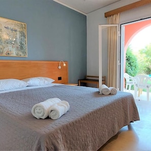 Camera d'albergo con un letto, un comodino, un quadro appeso al muro e vista sull'esterno tramite una porta in vetro.