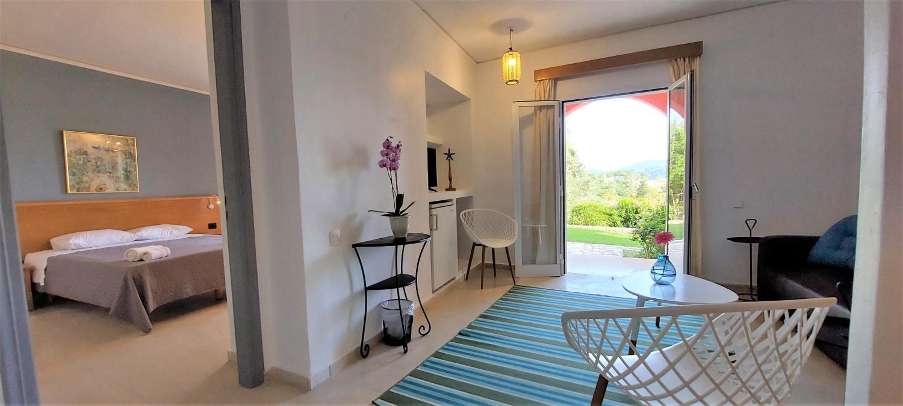 A hotel room with a bed, a desk, a chair, a small table, and a view of the outdoors.