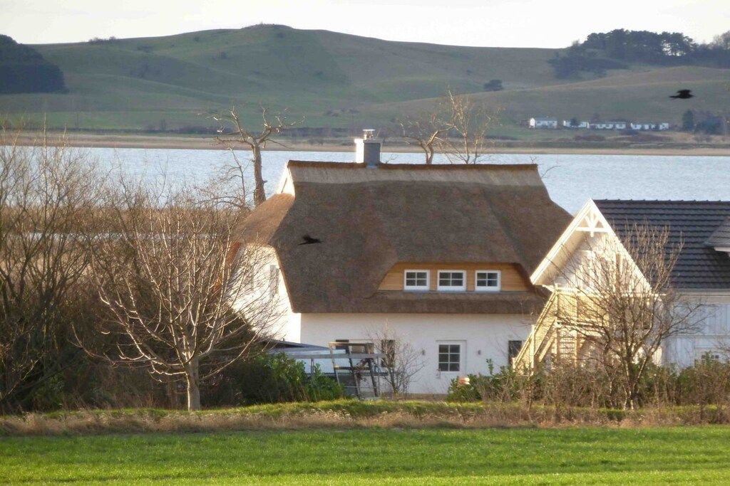 A house with a sloped roof, a chimney, and a view of a lake and hills in the background.
