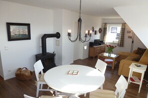 En hyggelig stue med et rundt hvidt bord, hvide stole, en sofa, en sort brændeovn og en lysekrone.