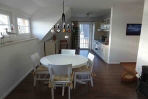 Ein Essbereich mit rundem Tisch und Stühlen, einer Chandelüster und Blick auf die Küche sowie den Wohnbereich.