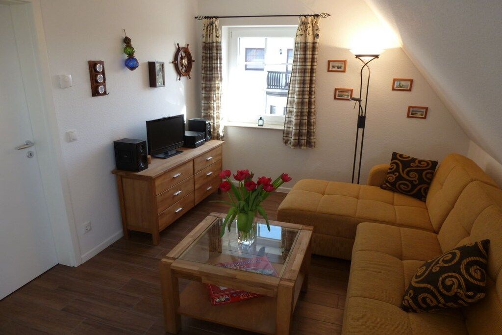Una sala de estar acogedora con un sofá, una mesa de centro con un florero, un televisor sobre un mueble de madera y una lámpara de pie.