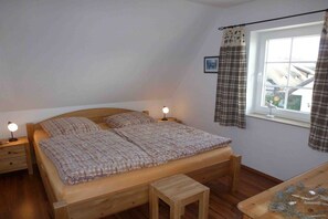 Ein Einzelbett mit Holzrahmen, zwei Nachttische mit Lampen, ein kleiner Hocker und ein Fenster mit Vorhängen.