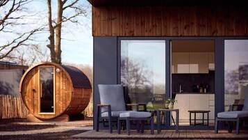 Een modern gebouw met een houten gevel, een groot houten vat en een zithoek met stoelen en een tafel.