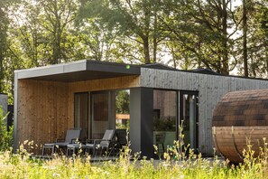 A modern, minimalist house with a wooden exterior, large glass windows, and a small patio with two chairs. - This Hofvilla Amalia for 2 pers. features a private sauna and offers the perfect combination of comfort and wellness. (Lattrop-Breklenkamp)